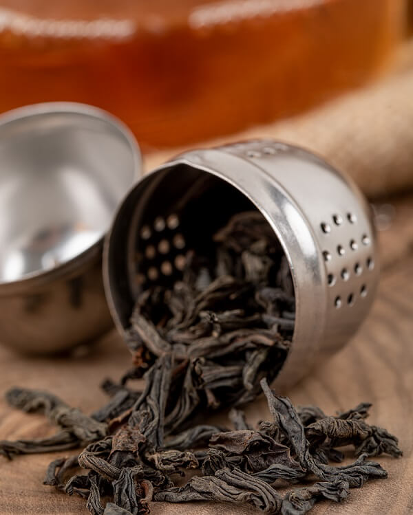 A glass of rich black tea beside loose tea leaves